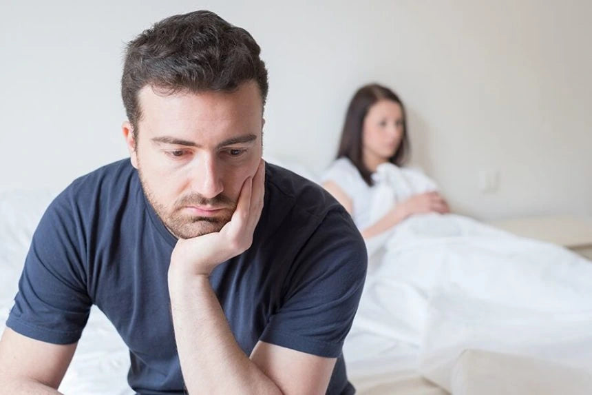 Hombre sentado en una cama con su pareja al fondo